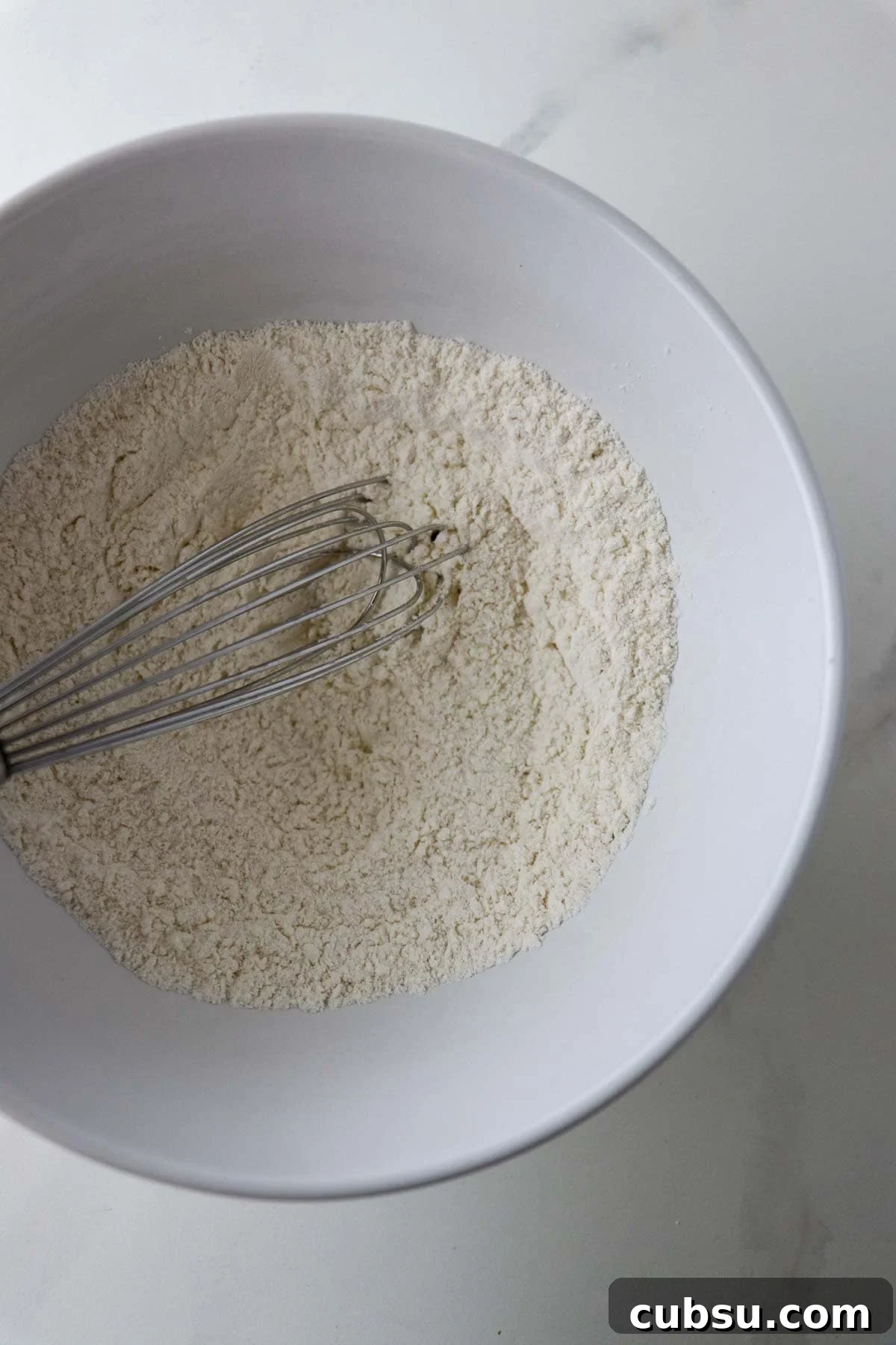 Flour in a white bowl with a whisk.