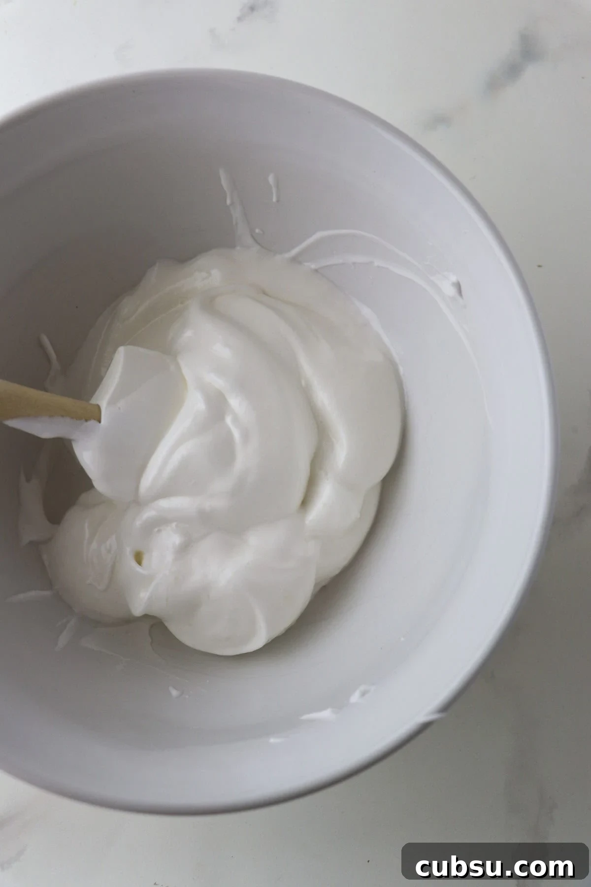 Whipped egg whites in a white bowl with a whisk.