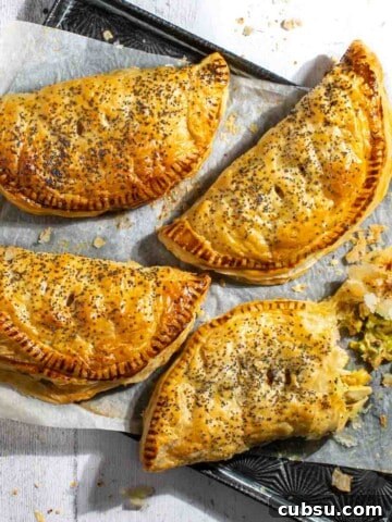 Four creamy chicken and leek pies on a baking sheet with one pie broken open.
