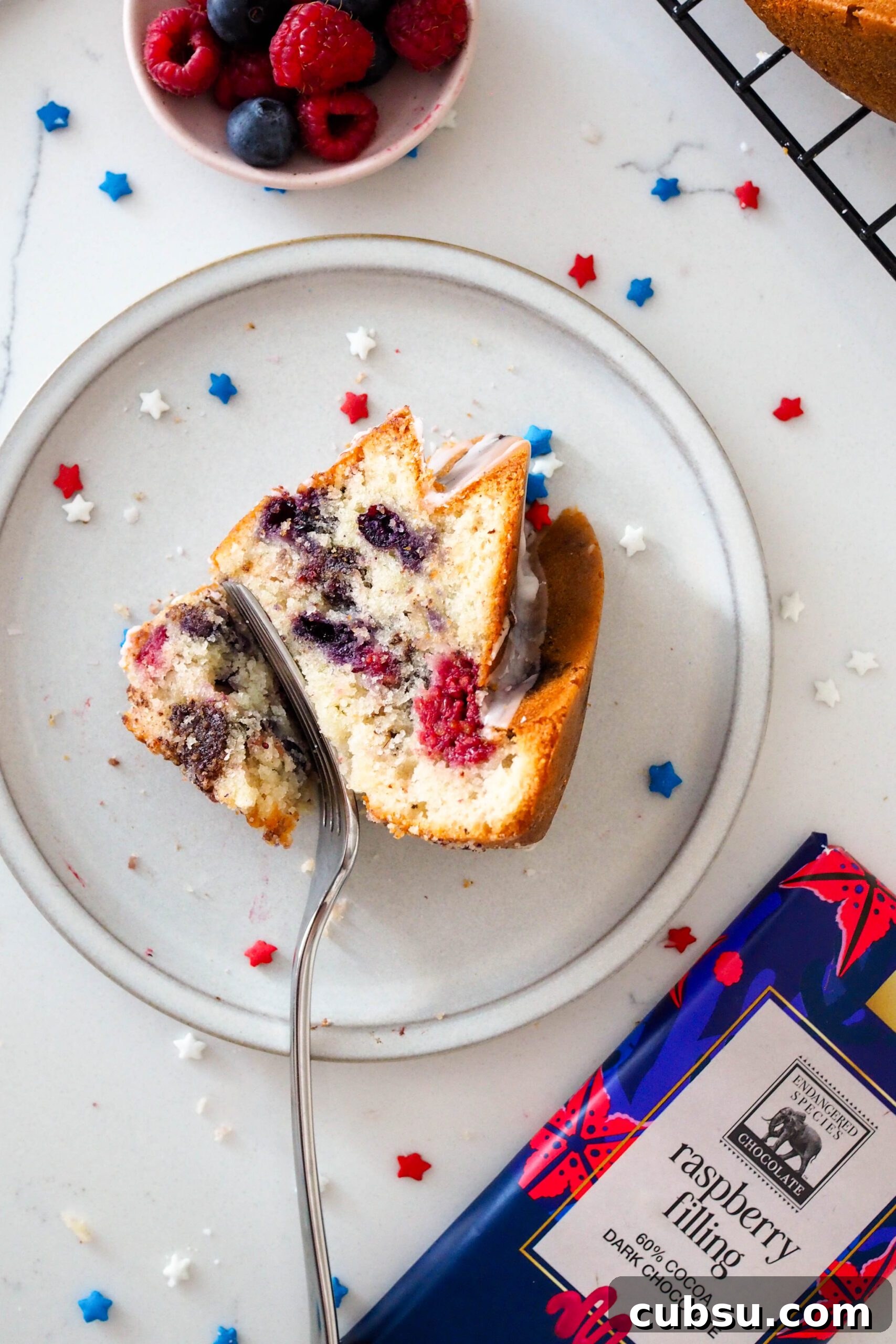 A slice of berry Bundt cake on a grey plate with red, white, and blue sprinkles around it.