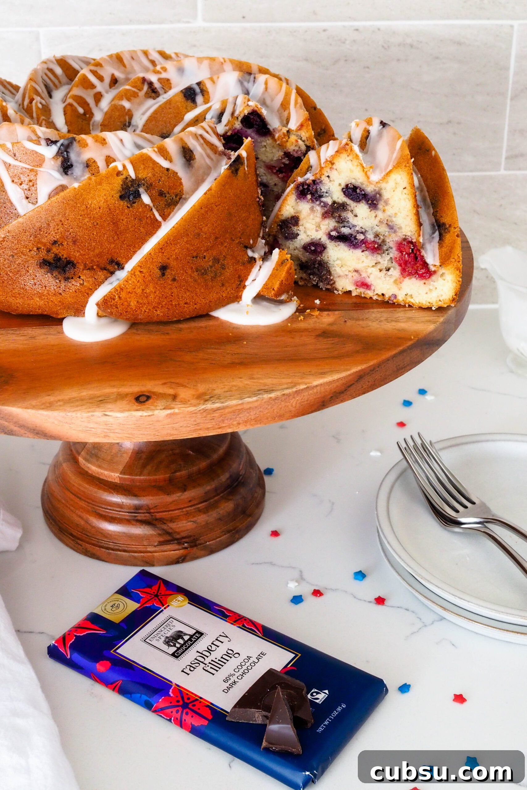 A slice is being removed from a berry Bundt cake on a cake stand.
