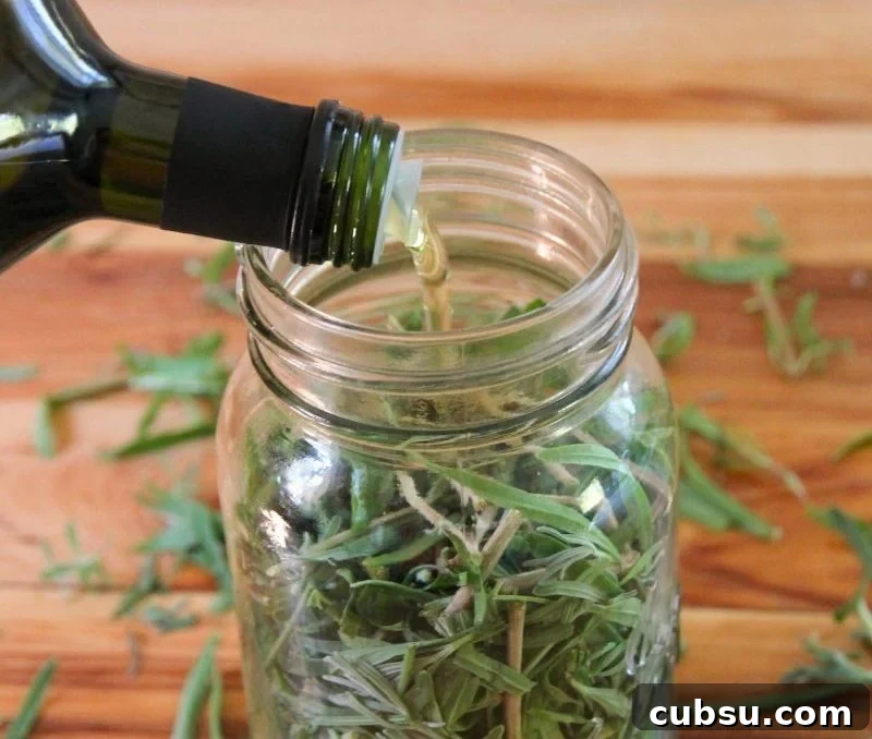 Pouring oil into a mason jar stuffed with fresh lavender buds and green leaves. 