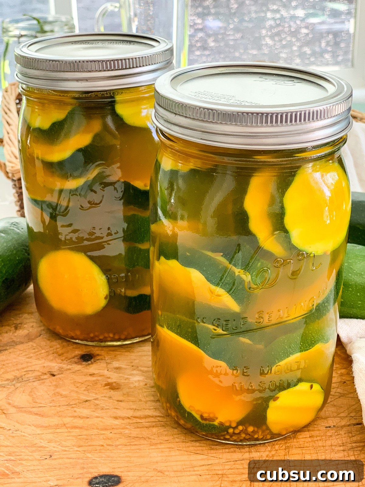 Quick Refrigerator Zucchini Pickles — No Canning Required 13 Two Mason jars filled with zucchini pickles on a cutting board.