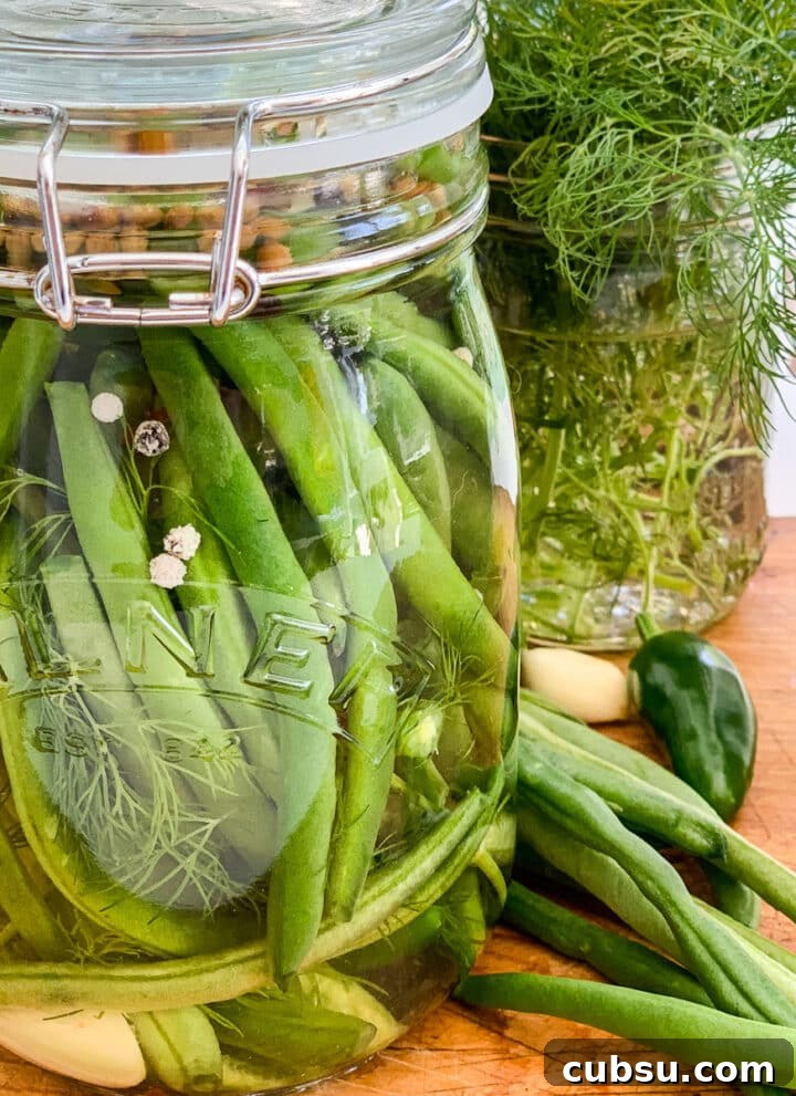 A clear glass jar filled with pickled green beans on a cutting board.