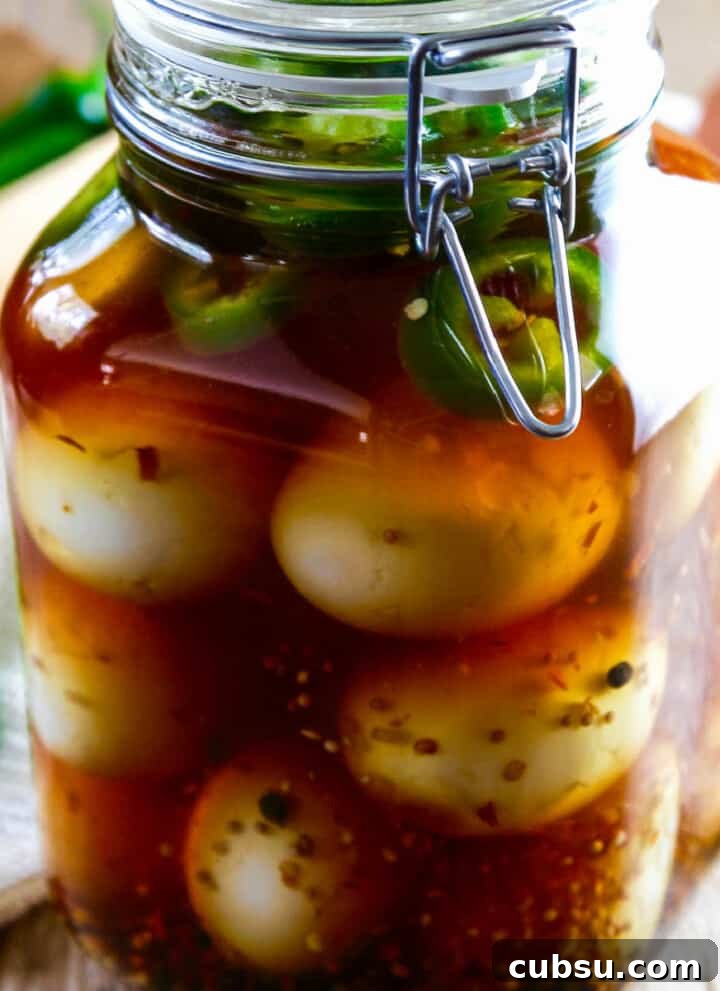 A large glass clamp jar filled with pickled eggs, fresh jalapeno slices, and spices.