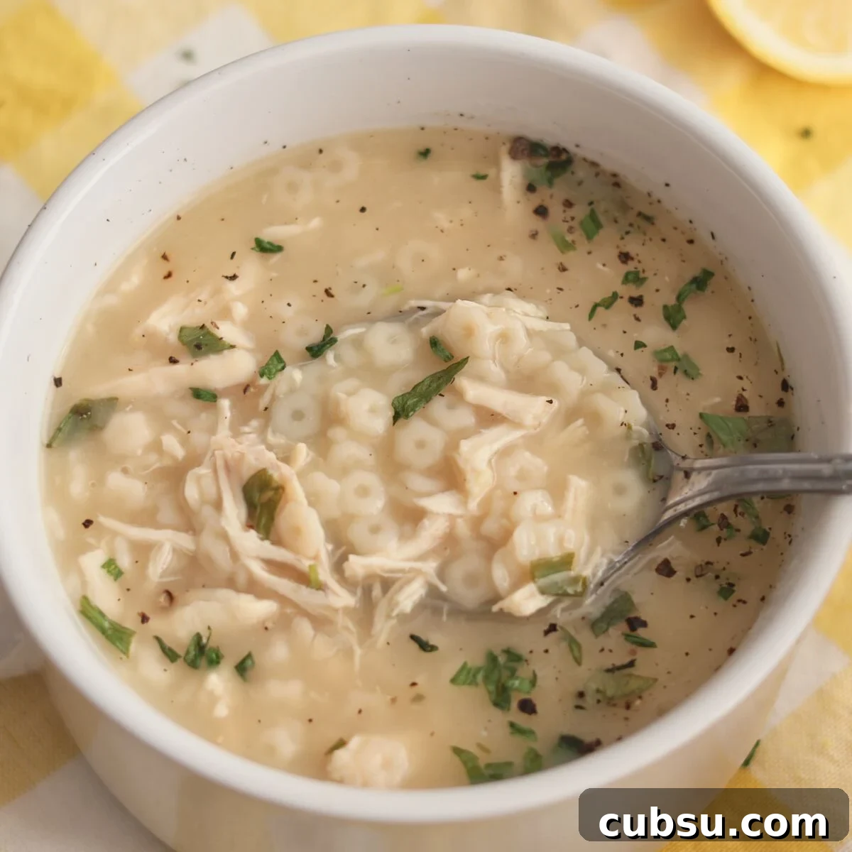 white bowl set on yellow checked napkin filled with chicken pastina soup and 