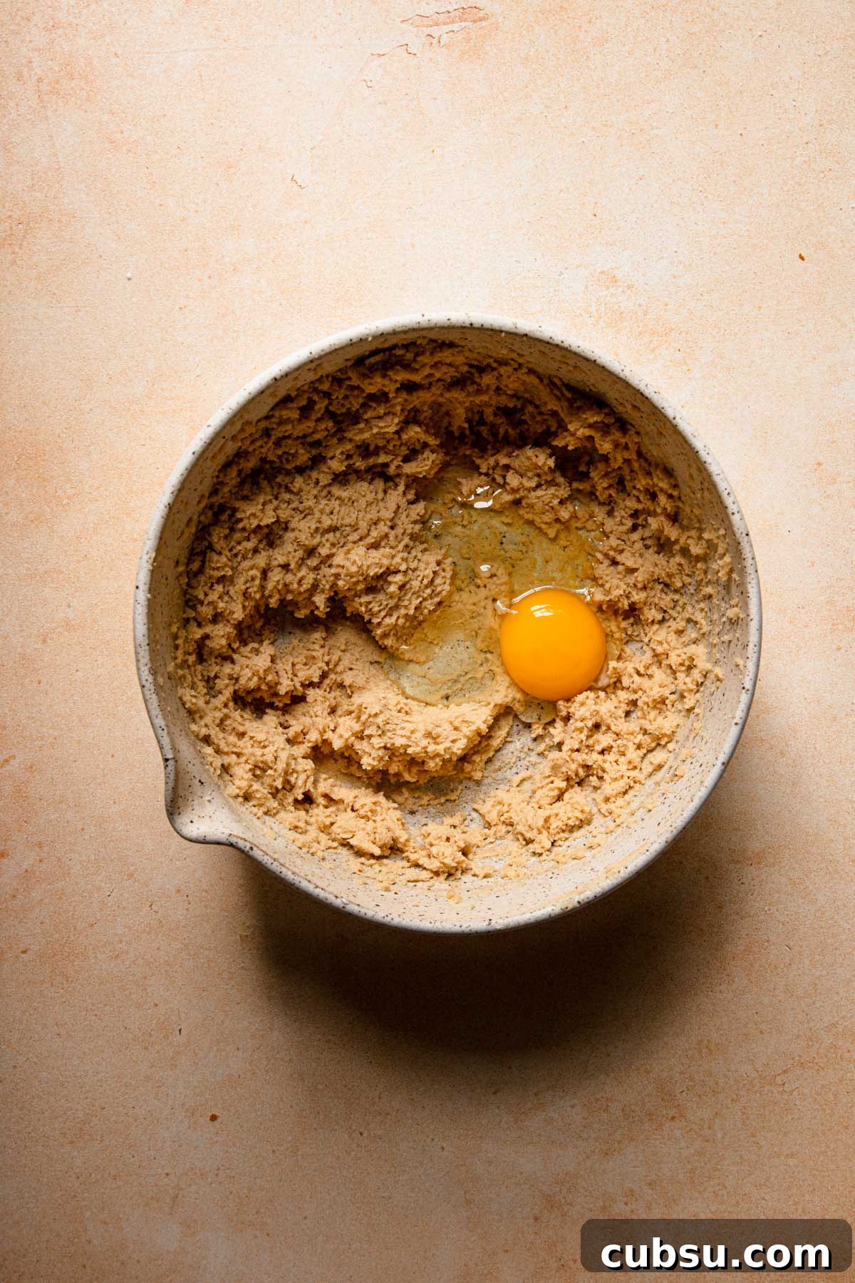 A mixing bowl with cream butter and an egg.