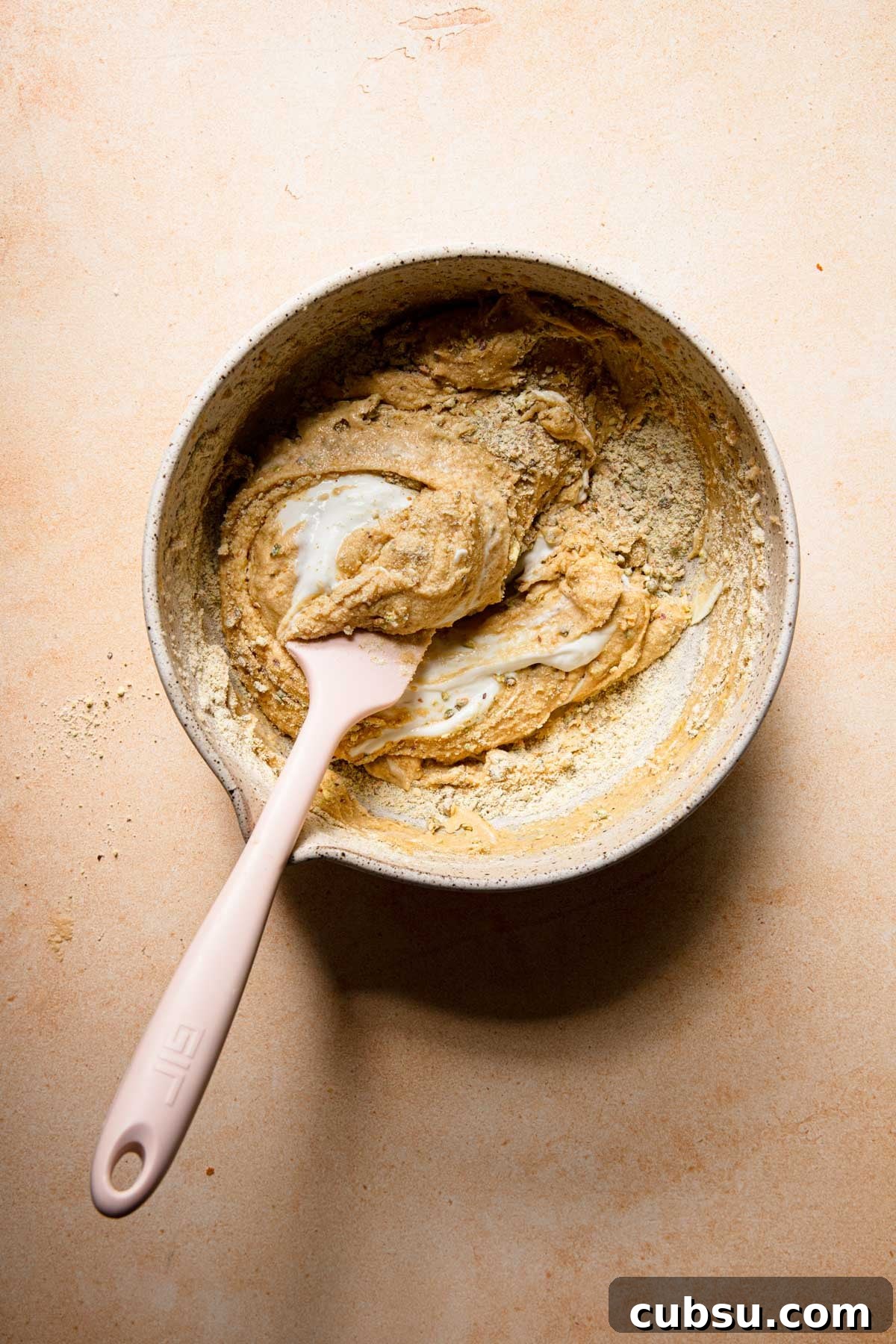 A mixing bowl with a cake butter folding cream with a spatula.
