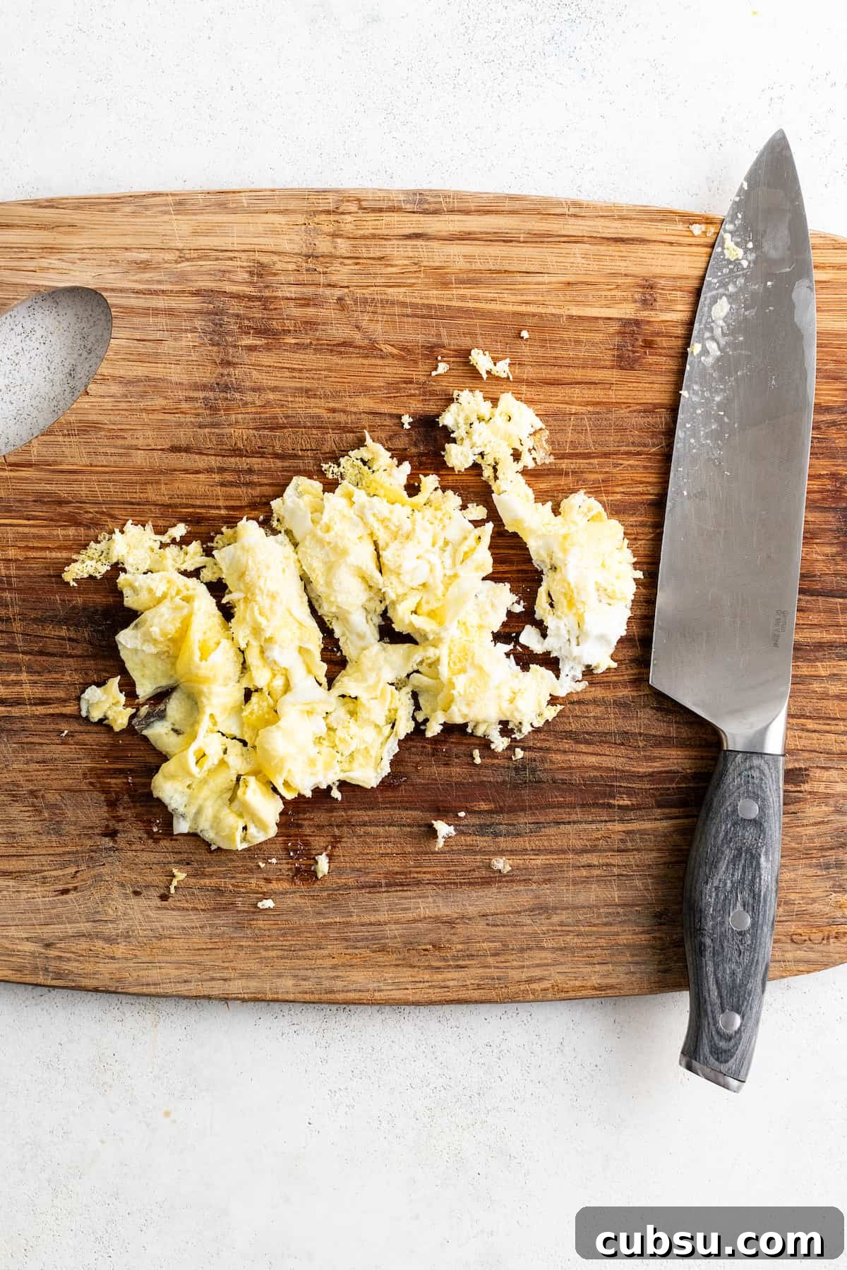 Chopping cooked scrambled eggs on a cutting board.