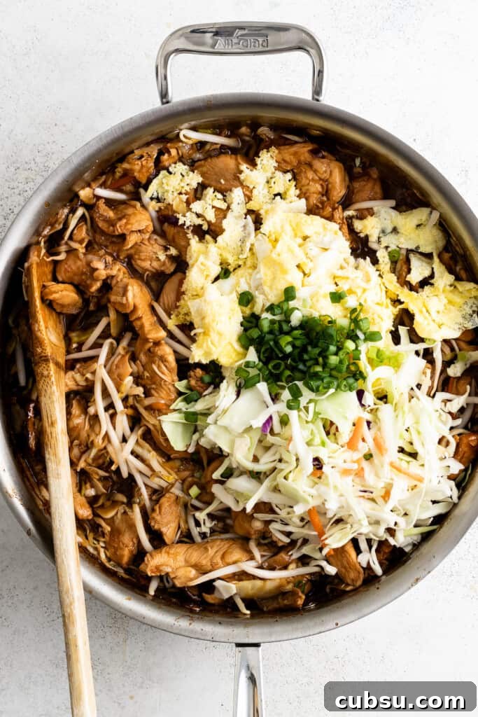 Adding cooked eggs, slaw, and scallions to moo shu chicken.