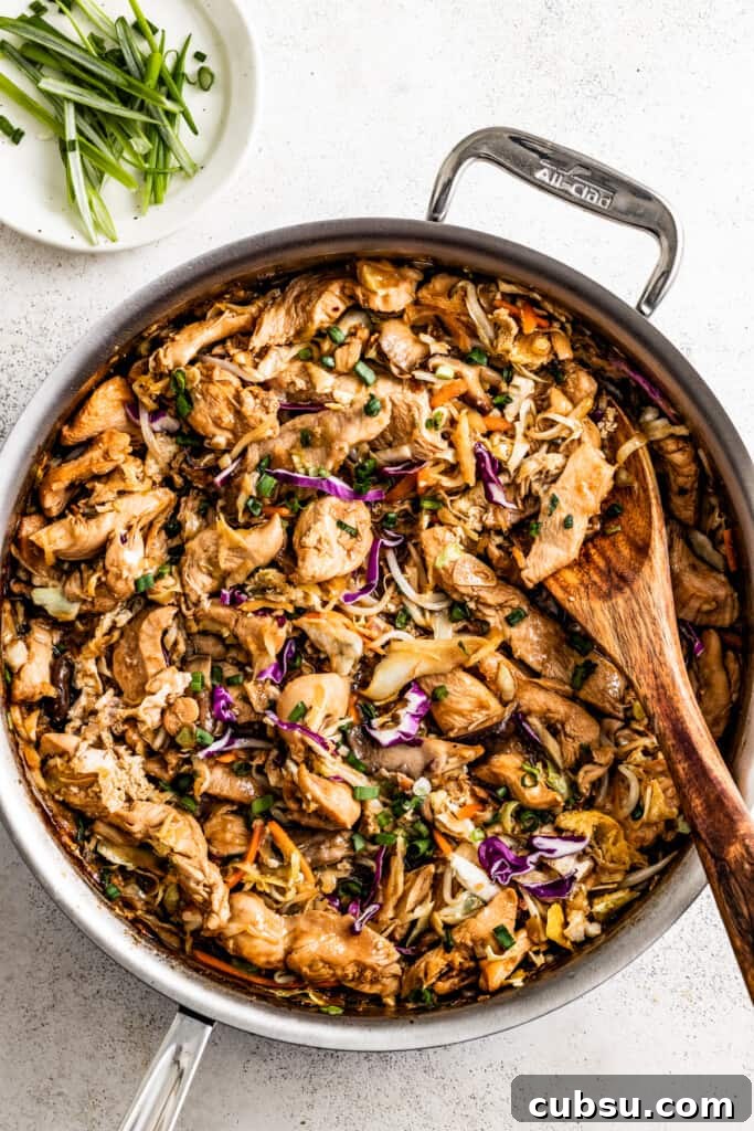 overhead shot of moo shu chicken in a skillet, with a wooden spoon stirring through it.