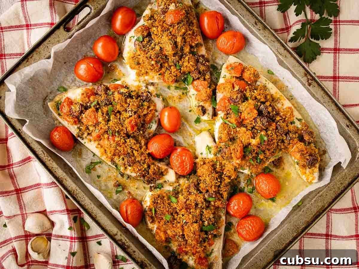Four breadcrumb topped swordfish steaks in a baking pan surrounded by cherry tomatoes.