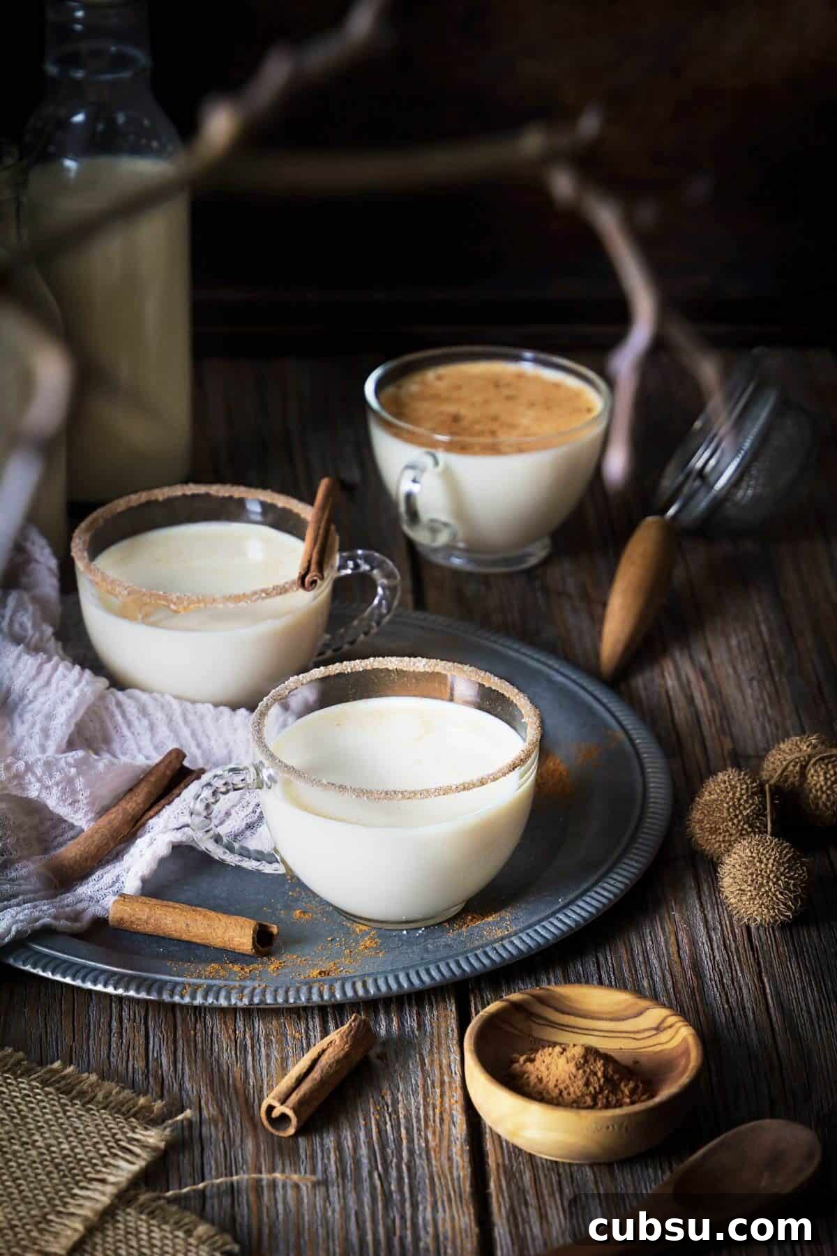 Melktertjies Milk Tart Cocktail Recipe: Creamy South African Drink 2 Three small glasses with milk tart cocktail on a rustic wooden table and cinnamon.