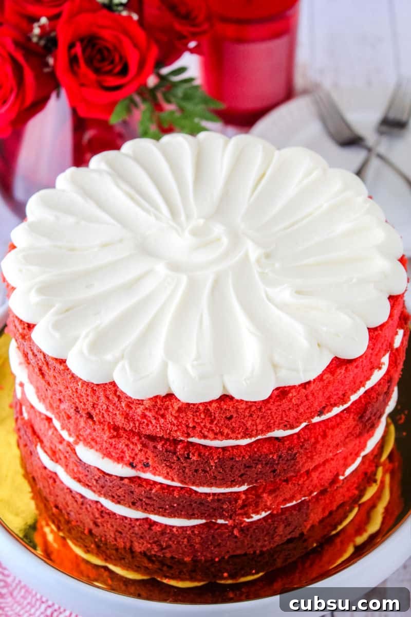 red velvet cake on a cake stand next to red roses, candle, plates, and forks