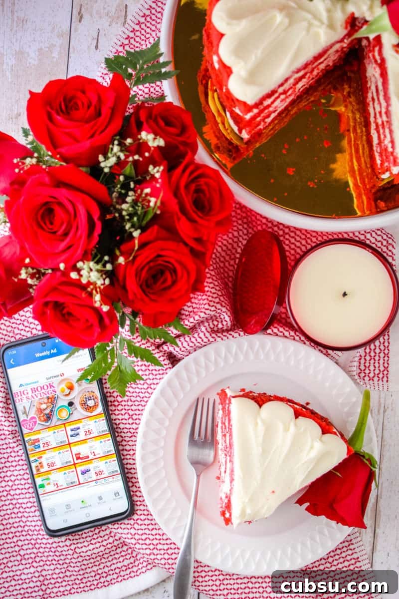 looking down at a bouquet of roses, slice of red velvet cake on a plate with a fork and a rose, a red candle, and smartphone with Albertsons app opened up