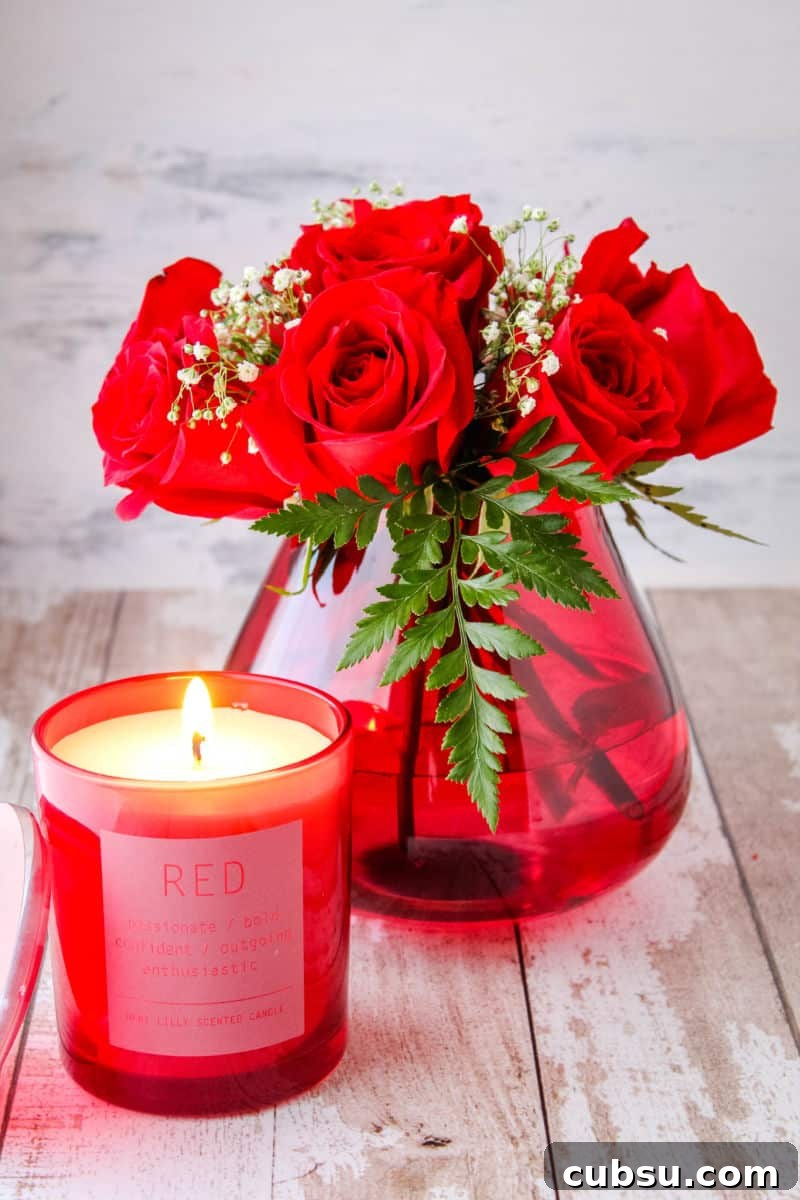 small bouquet of red roses in a red teardrop vase next to a red candle