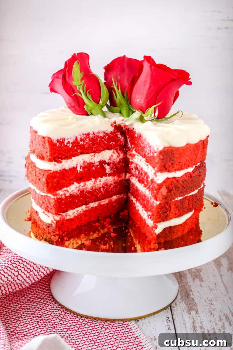 red velvet cake on a cake stand topped with fresh roses with a slice cut out to show layers