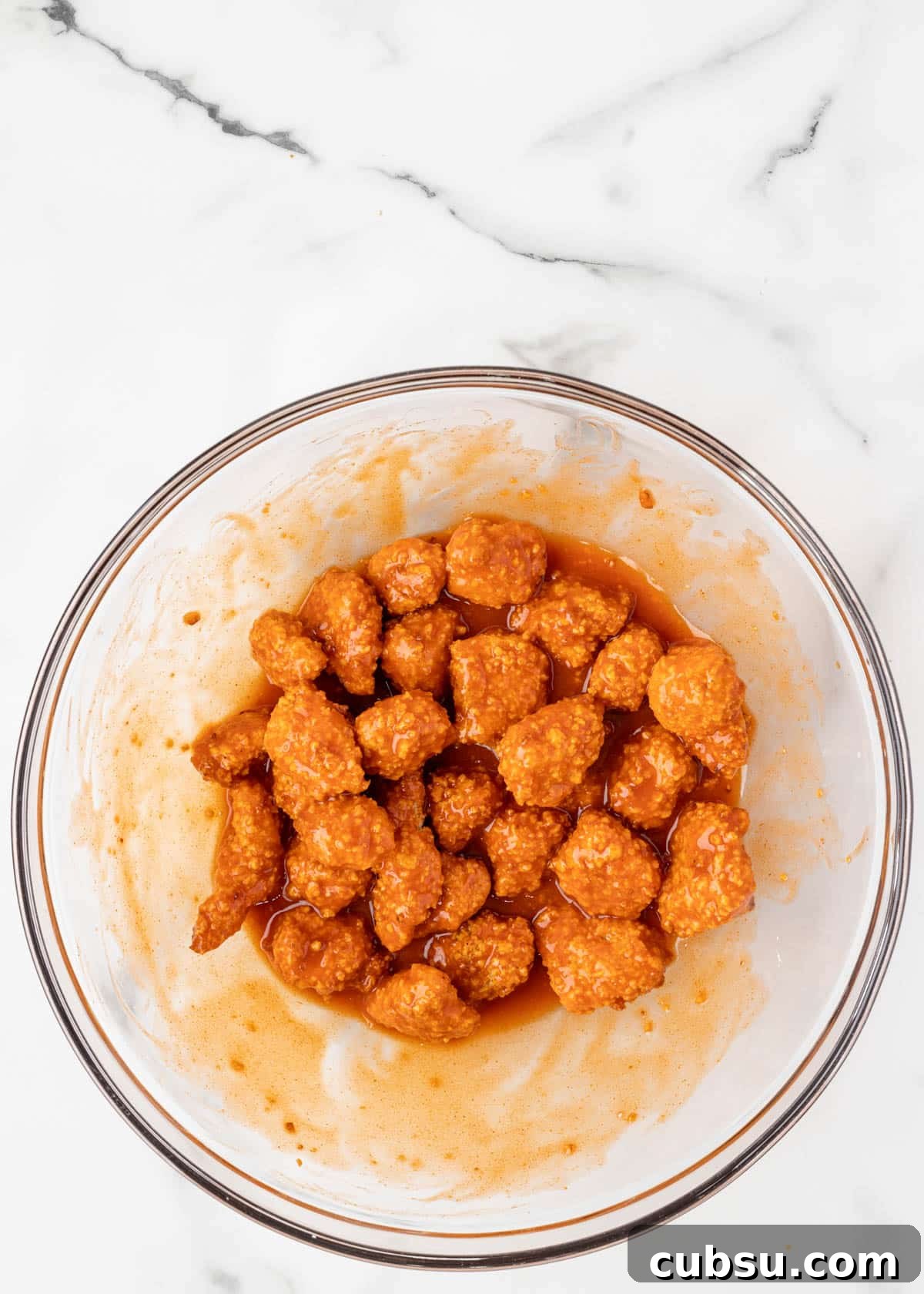 air fried buffalo chicken bites tossed in buffalo sauce in a glass bowl on a white marble board