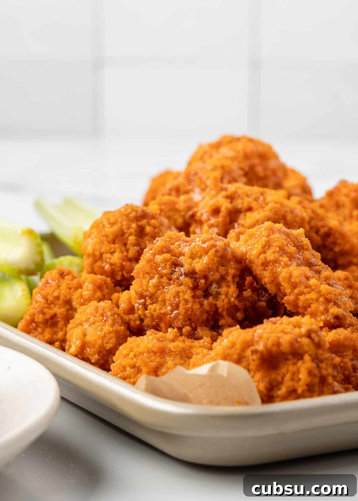 air fryer buffalo chicken piled onto a parchment lined baking sheet with celery sticks behind them