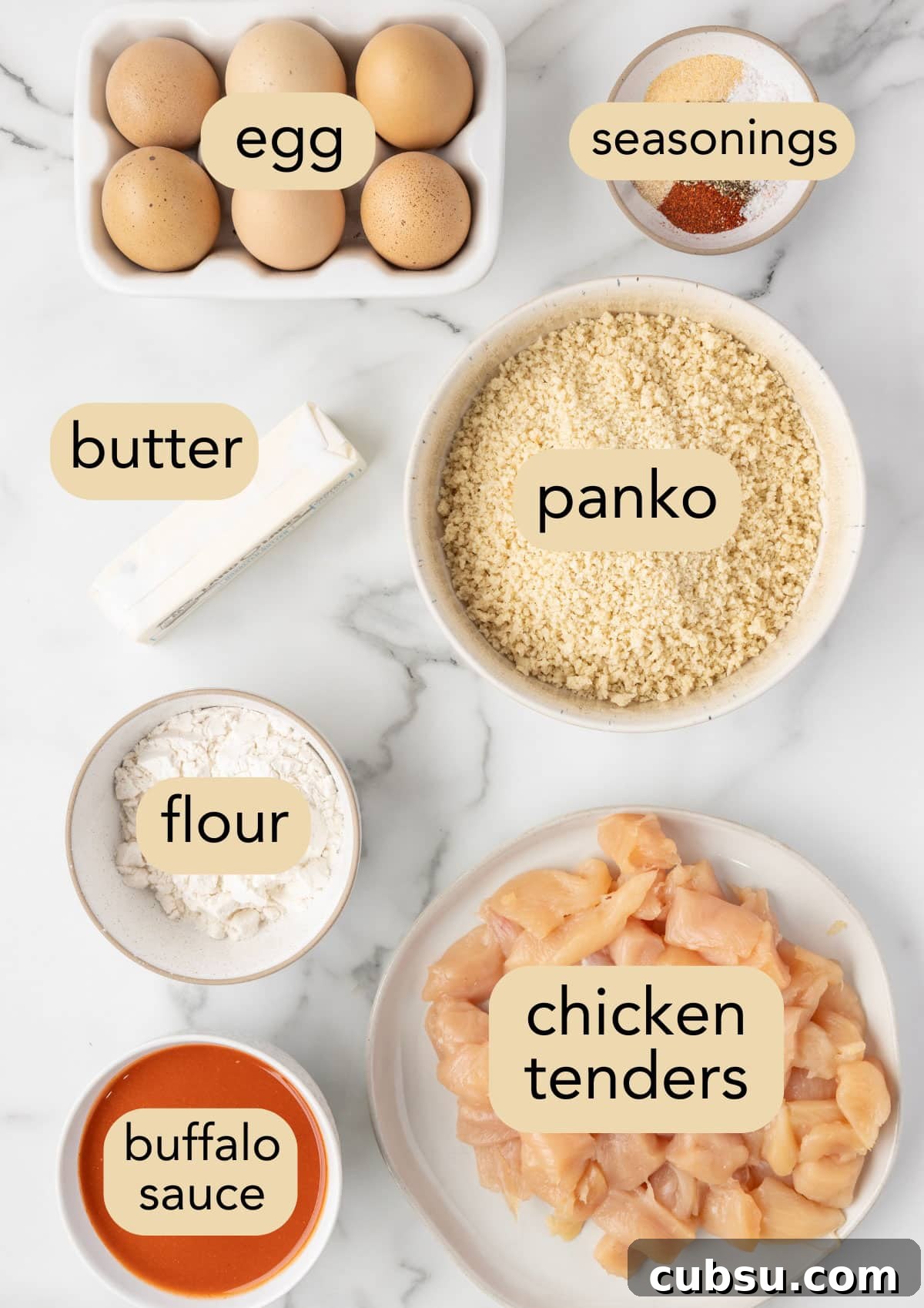 overhead of ingredients needed to make air fryer buffalo chicken bites in bowls on a white marble board with text label overlays