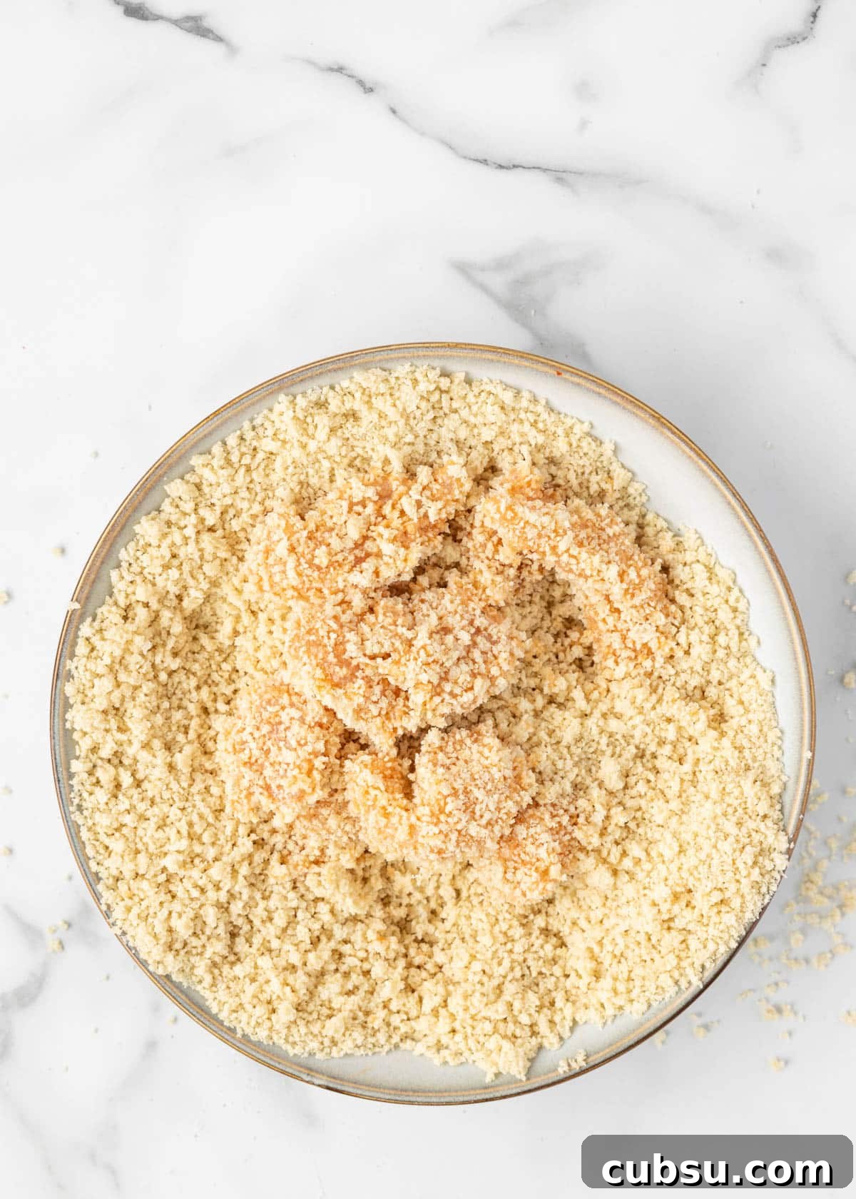 boneless chicken cubes breaded in seasoned panko in a bowl on a white marble board