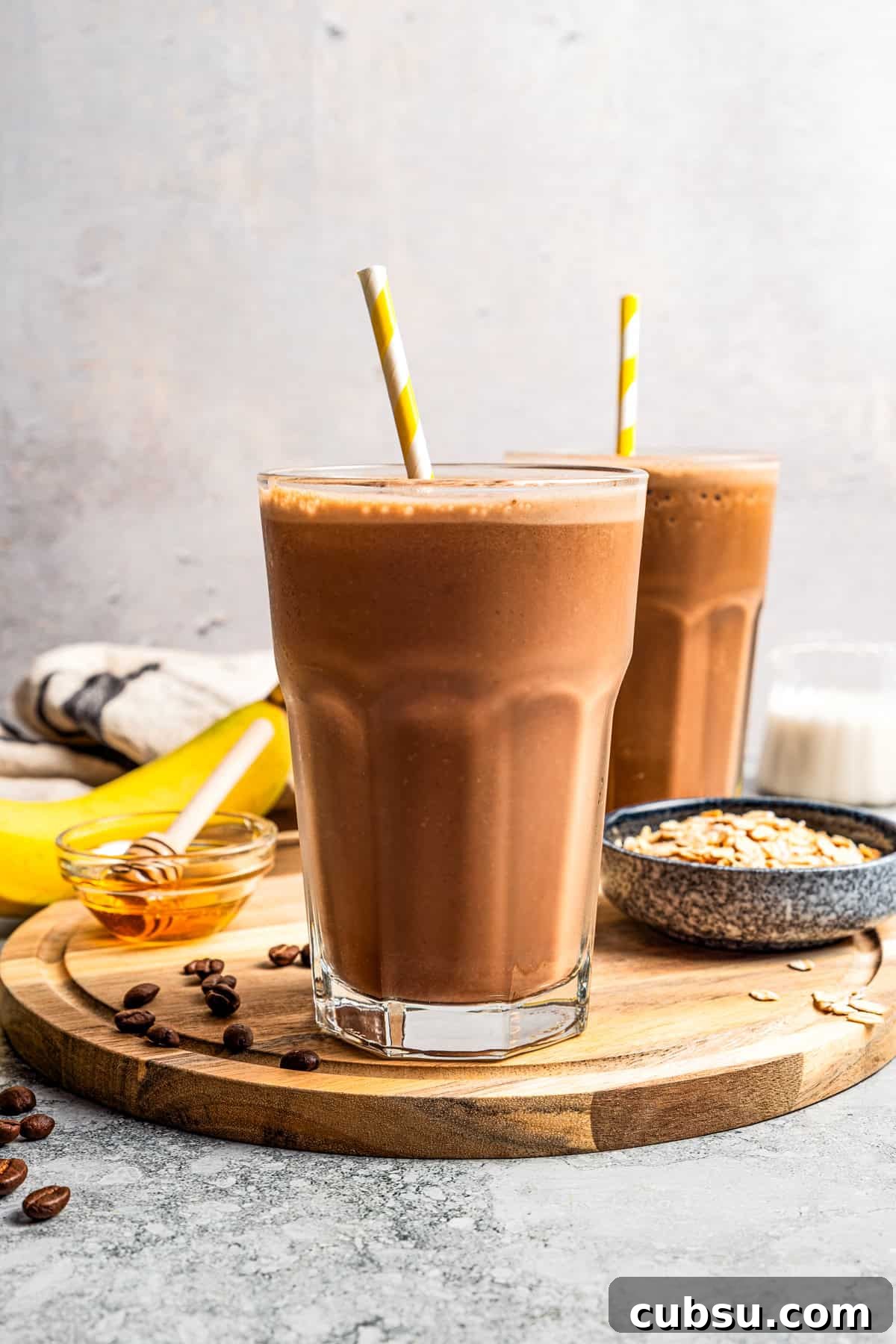 This creamy coffee smoothie is a delicious and energizing way to start busy mornings! It’s made with oats, flaxseed, and bananas for a creamy, filling texture. A coffee smoothie in a tall glass with a straw and a second smoothie in the background.