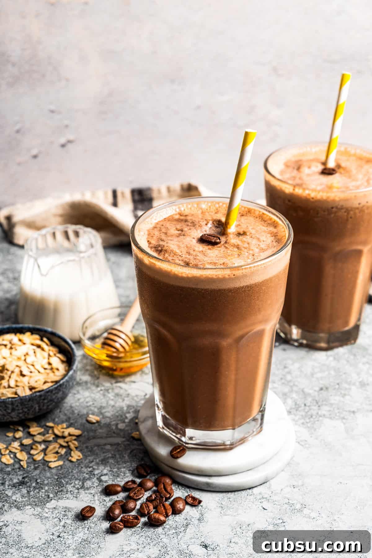 This creamy coffee smoothie is a delicious and energizing way to start busy mornings! It’s made with oats, flaxseed, and bananas for a creamy, filling texture. A coffee smoothie in a tall glass with a straw and a second smoothie in the background.
