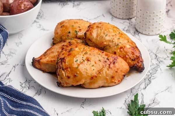 Golden glazed chicken breasts, on a white plate sprinkled with dried parsley on a marble table.