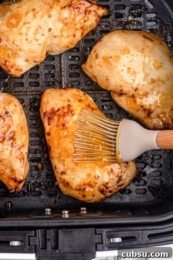 Chicken in the air fryer basket being brushed with peach glaze.