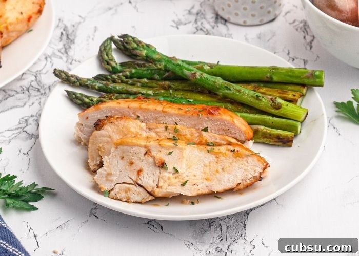 Sliced chicken breast served on a white plate with green asparagus.