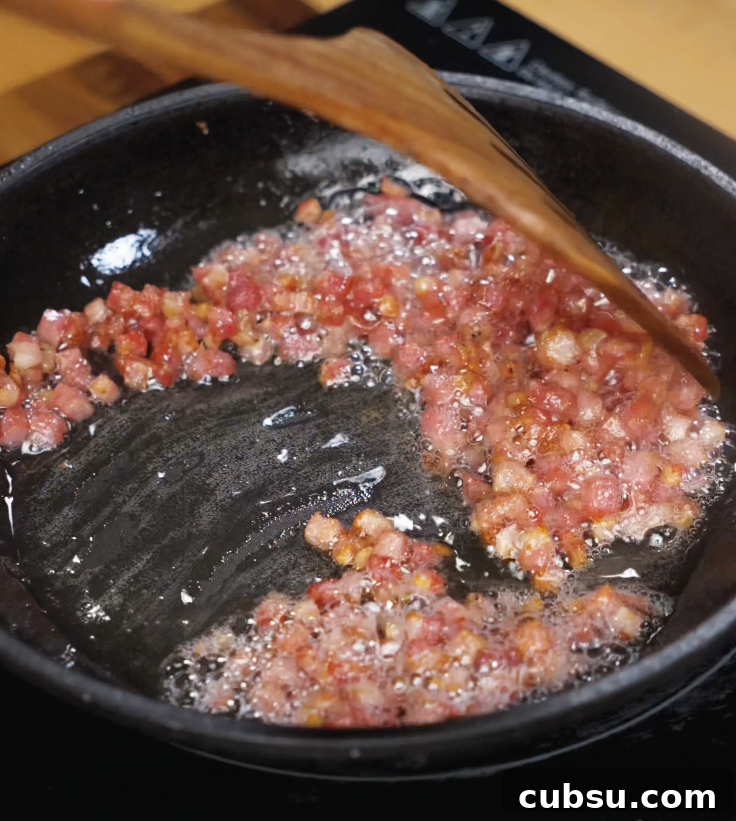 Diced pancetta is rendered in a skillet until crispy and golden, releasing its rich, savory fat.