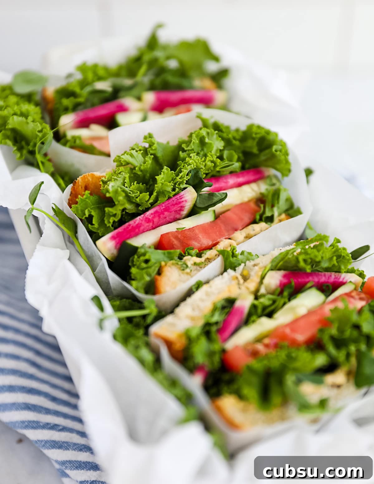 Wrapped veggie sandwiches including bread, hummus, lettuce, cucumber, radishes, and tomatoes.