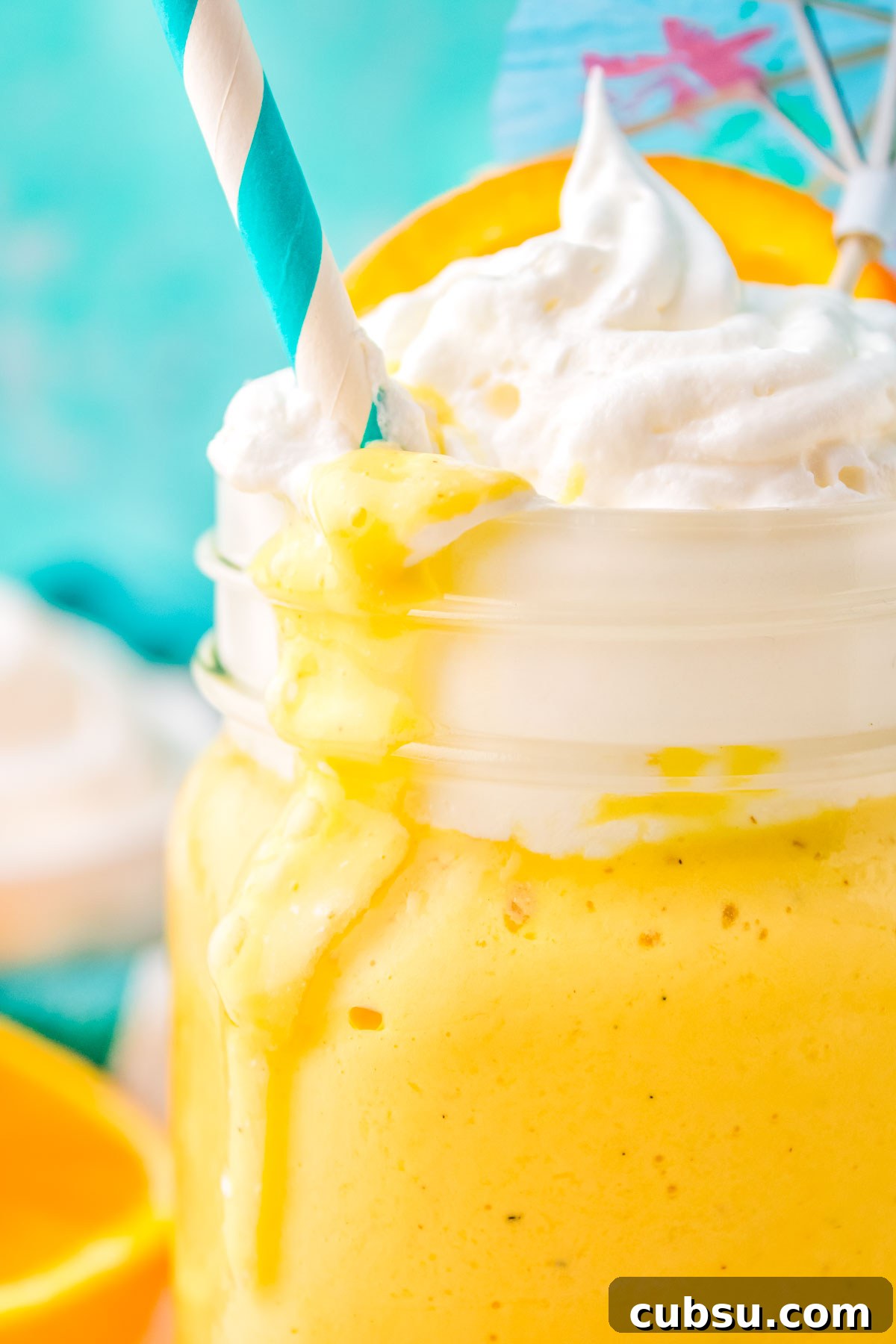 An Orange Creamsicle Milkshake poured into a glass and topped with whipped cream and a straw. 