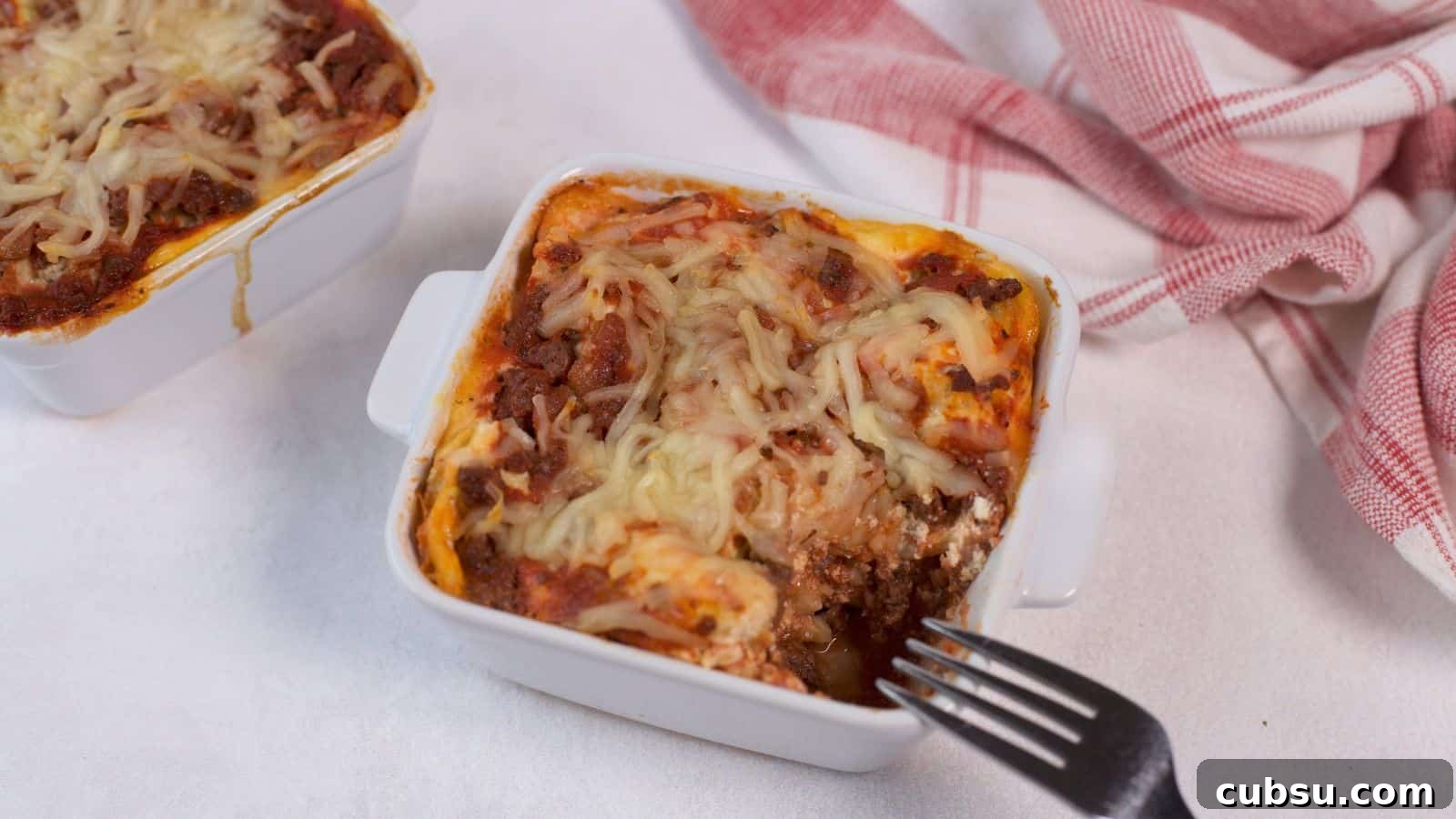 17 Timeless Grandma Recipes You Need to Try Now 16 Two square ceramic dishes of baked lasagna with melted cheese on top, next to a red and white checkered napkin, on a light textured surface.