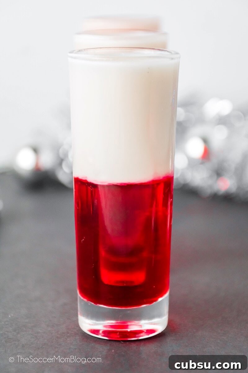 Festive Tipsy Santa Shooters Recipe for Holiday Parties 5 row of shot glasses filled with red and white layered drink