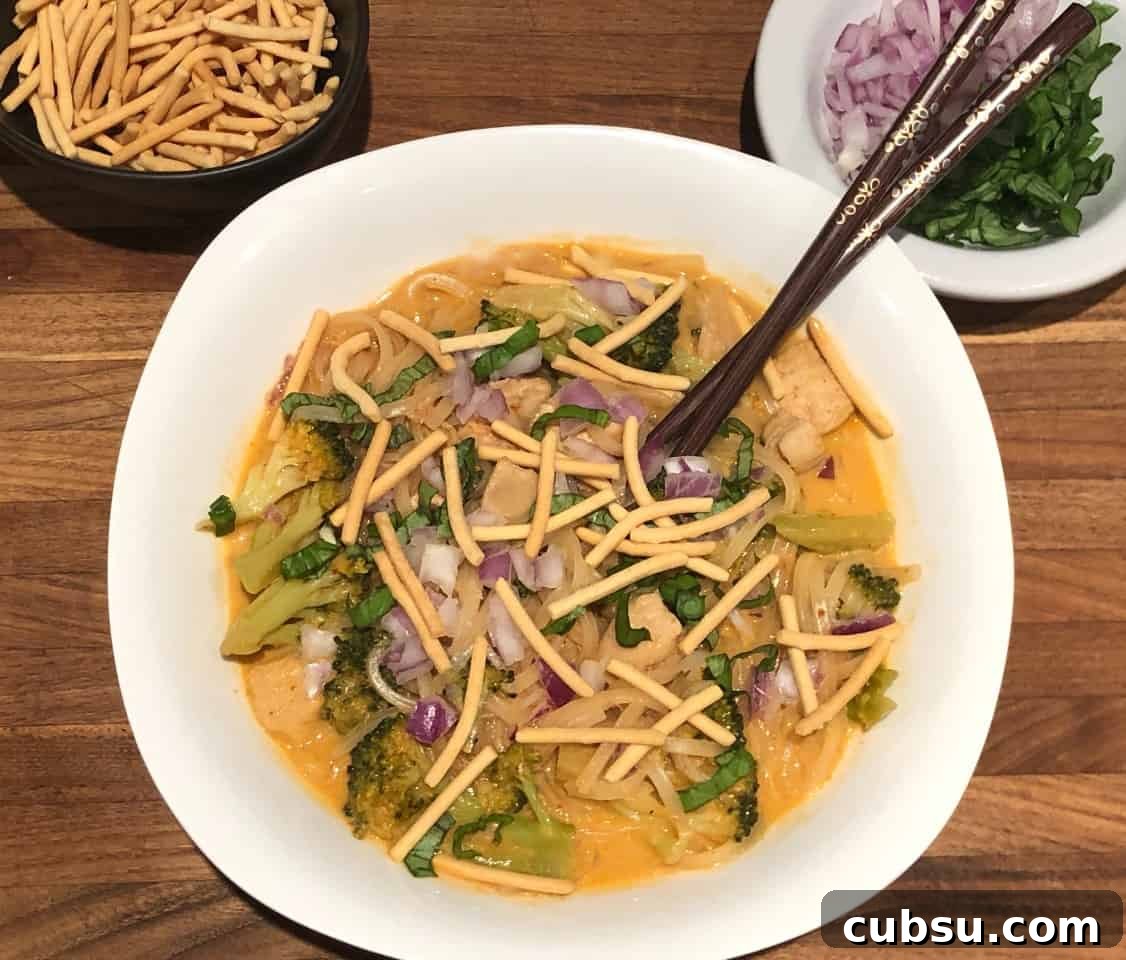 thai red curry soup with noodles and chow mein and red onion on top.