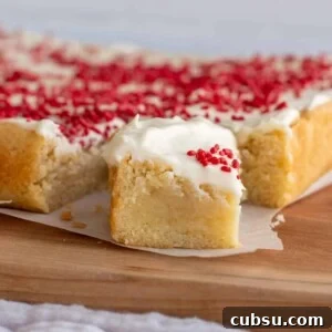 Sourdough Sugar Cookie Bars Recipe — Buttery Soft Cookie Bars 11 A sugar cookie bar sitting on parchment paper on a wooden board.