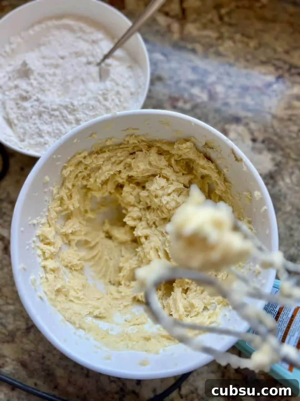 Sourdough Sugar Cookie Bars Recipe — Buttery Soft Cookie Bars 5 A bowl of wet ingredients with a mixer and bowl of dry ingredients behind the mixer.