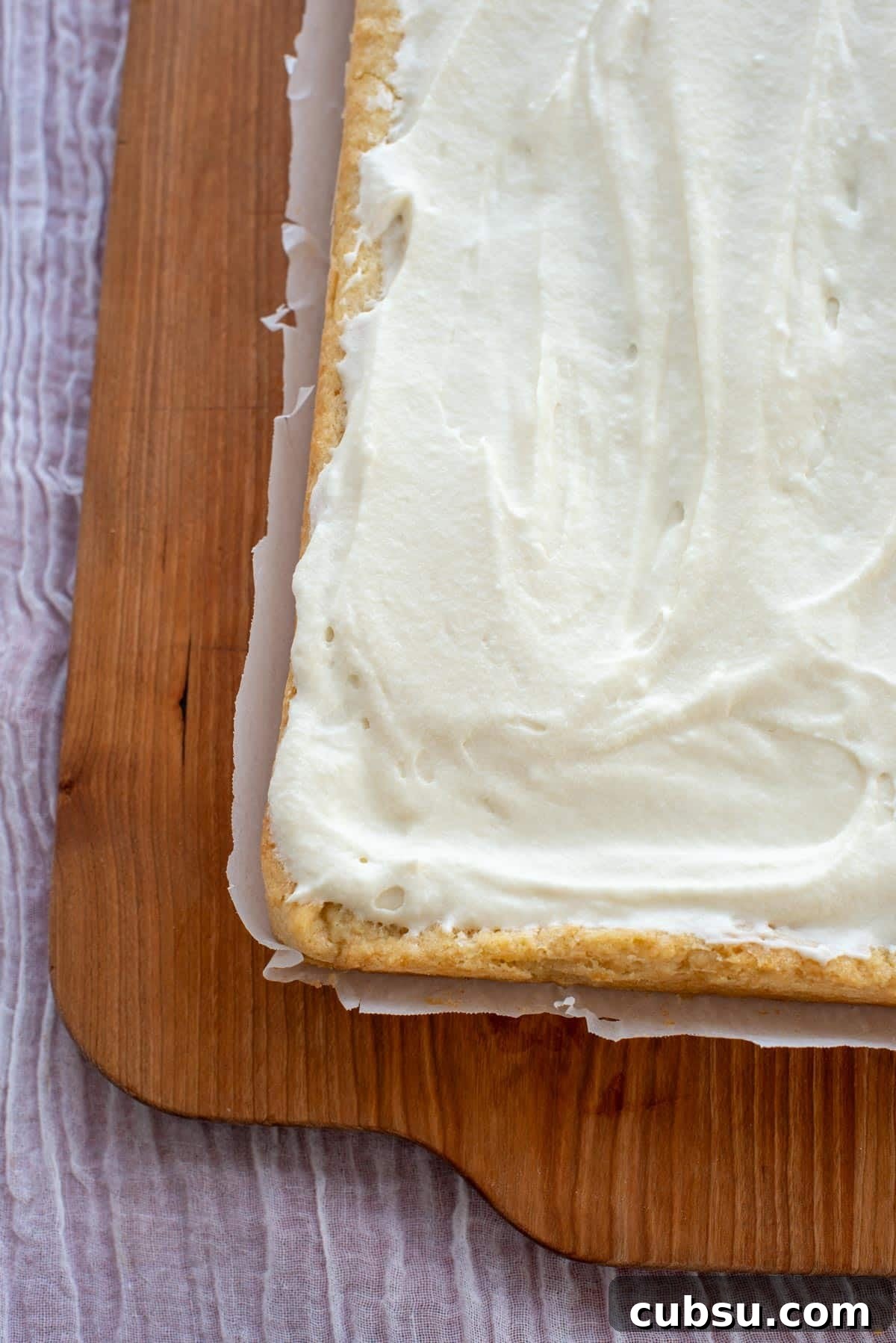 Sourdough Sugar Cookie Bars Recipe — Buttery Soft Cookie Bars 8 A block of sugar cookie bars covered in frosting sitting on a wooden board.