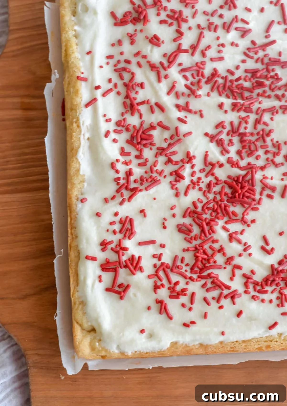 Sourdough Sugar Cookie Bars Recipe — Buttery Soft Cookie Bars 9 A block of sugar cookie bars covered in frosting and sprinkles and sitting on a wooden board.