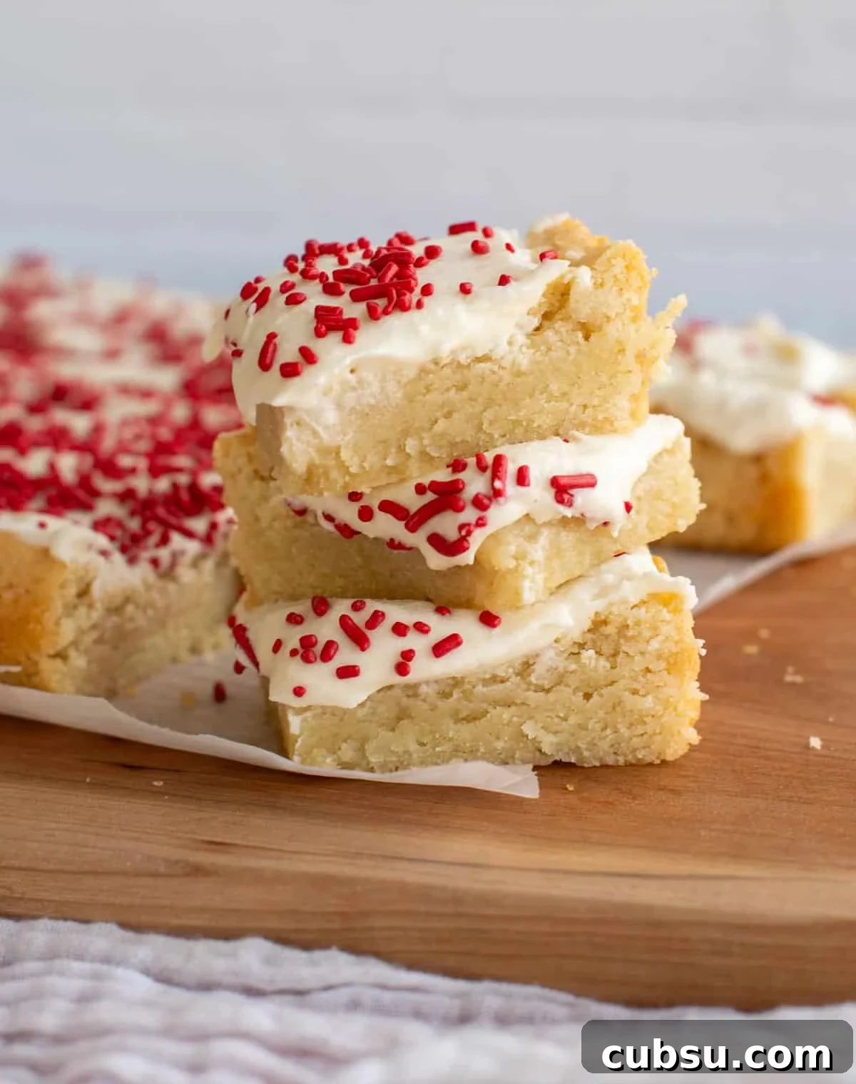 Sourdough Sugar Cookie Bars Recipe — Buttery Soft Cookie Bars 10 A stack of sourdough sugar cookie bars with sprinkles on top sitting on parchment paper.