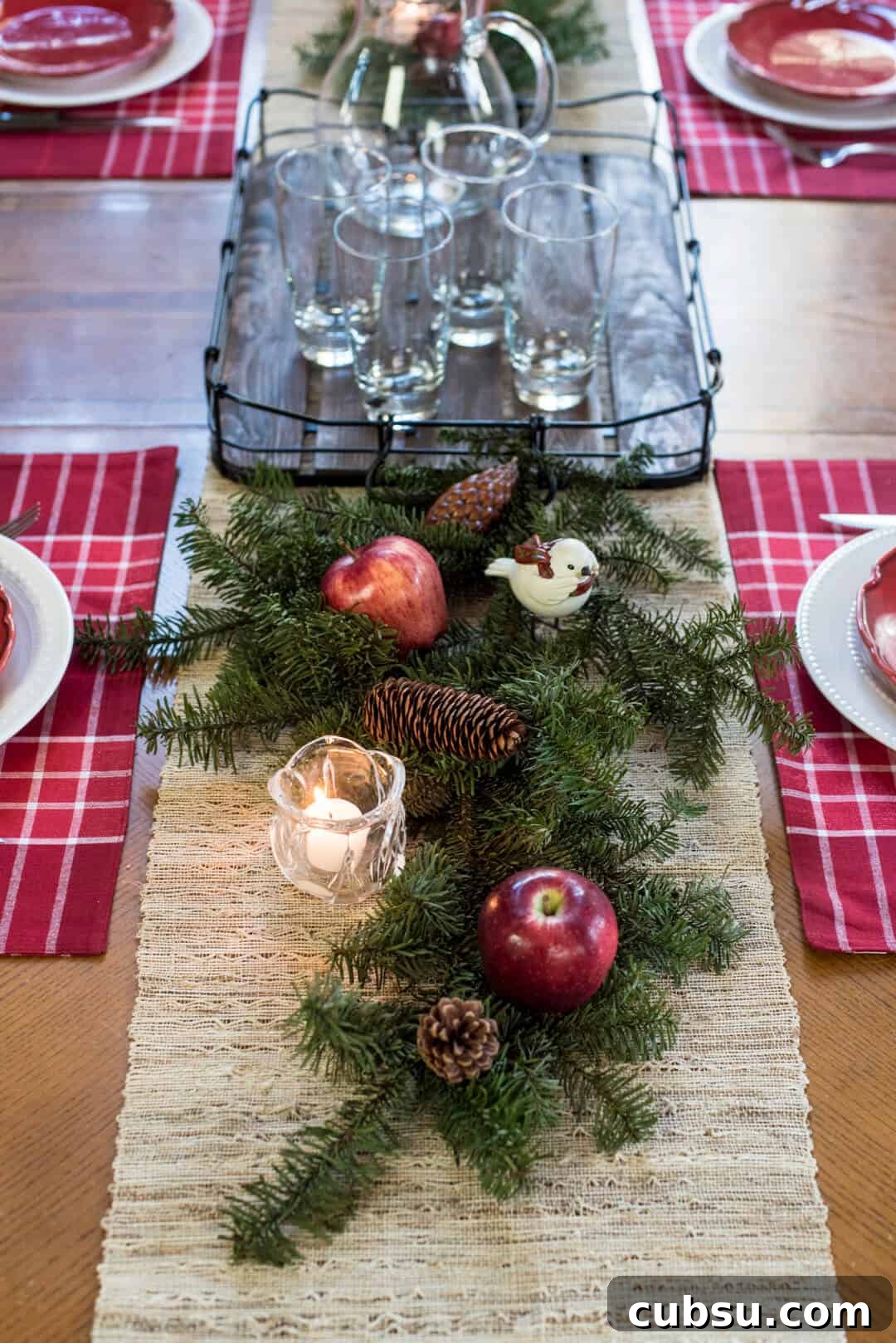 A pretty holiday tablescape with pine branches, pine cones, apples, birds, and candles.