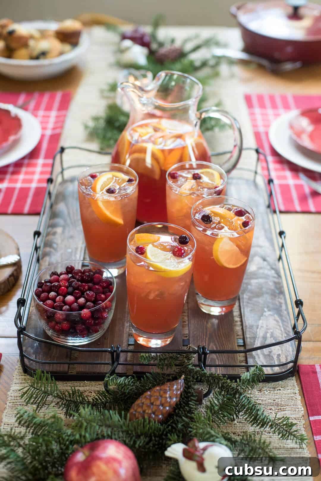 A wooden tray on a table with iced tea in glasses and a pitcher next to a bowl of cranberries.