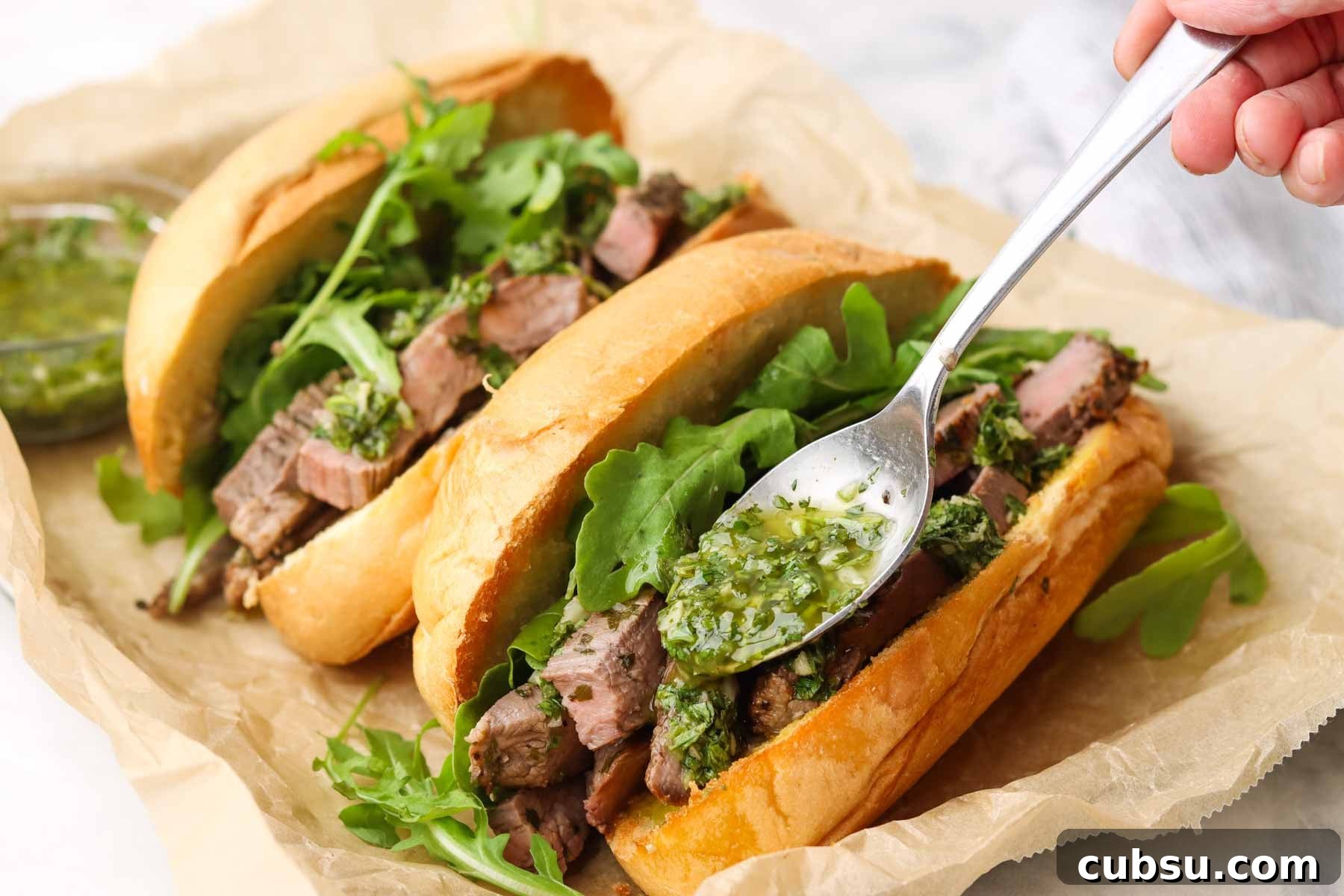 Juicy Steak Sandwich with Fresh Chimichurri Sauce 3 adding chimichurri with a spoon on a sandwich on a platter