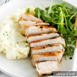 Juicy Grilled Boneless Pork Chops with Garlic Herb Marinade 6 sliced bonless pork chop on a plate with arugula and mashed potatoes