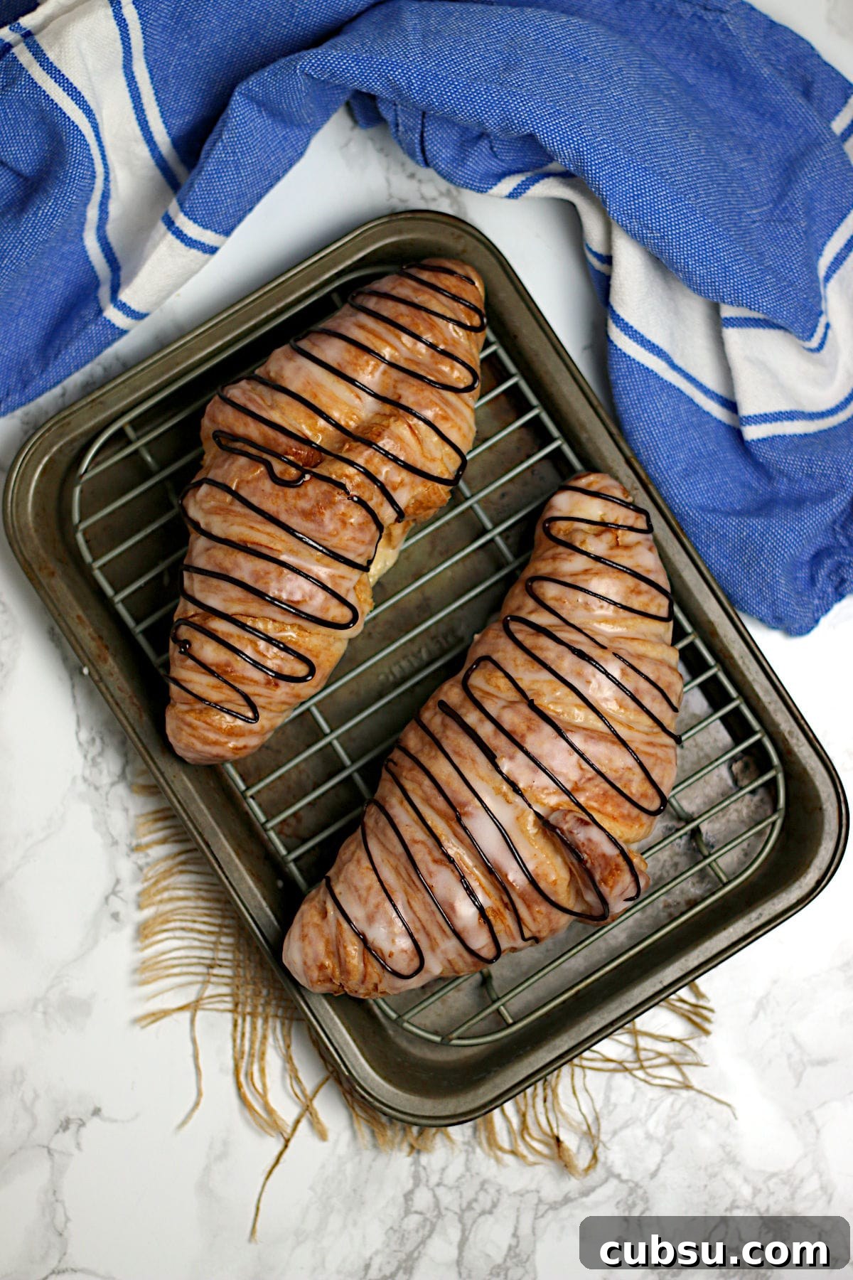An overhead photo of two chocolate drizzled Glazed Croissants on a small baking sheet.