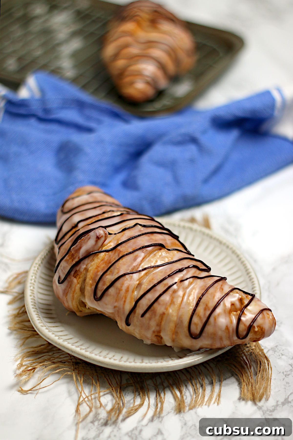 A chocolate drizzled glazed croissant on a small white plate.