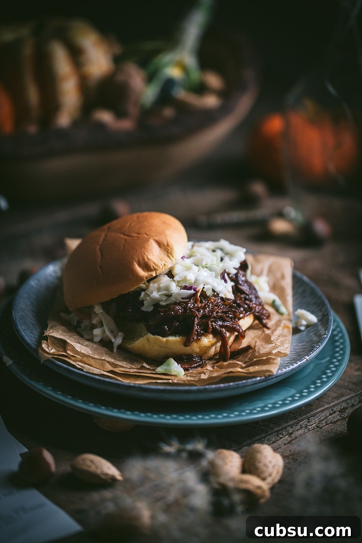shredded bbq beef sandwich topped with coleslaw on soft bun surrounded by fall imagery