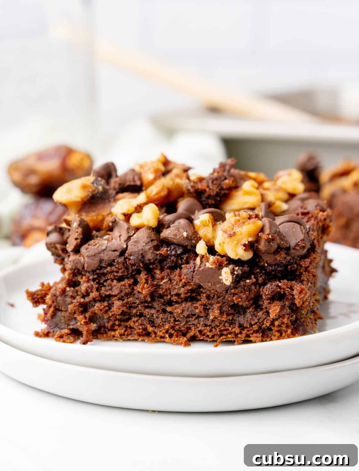 Decadent Chocolate and Date Cake Recipe for Moist Loaves 11 Frontal view of walnut chocolate chip topped date cake on a stack of white plates.