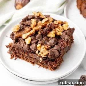 Decadent Chocolate and Date Cake Recipe for Moist Loaves 17 Square of chocolate chip walnut date cake on stack of two white plates. White surface, kitchen towel, loose dates around.